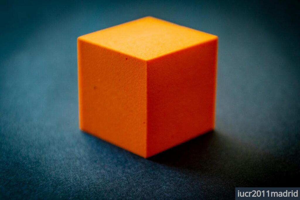 Close-up of an orange foam cube on a dark surface, highlighting its texture and color contrast.